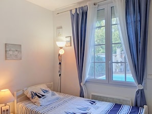 Un dormitorio con una cama, una lámpara de noche, una ventana con cortinas y un cuadro colgado en la pared.