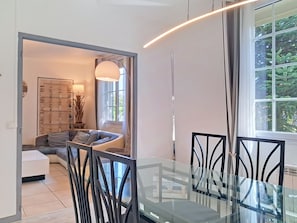 Un comedor moderno con una mesa de vidrio y sillas negras, un sofá con cojines, una lámpara y vistas a zonas verdes al exterior.
