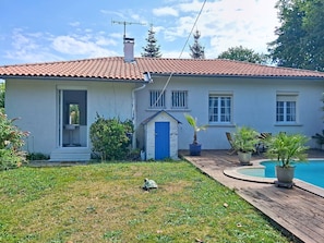 A house with a tiled roof, a small front porch, a swimming pool, and potted plants.