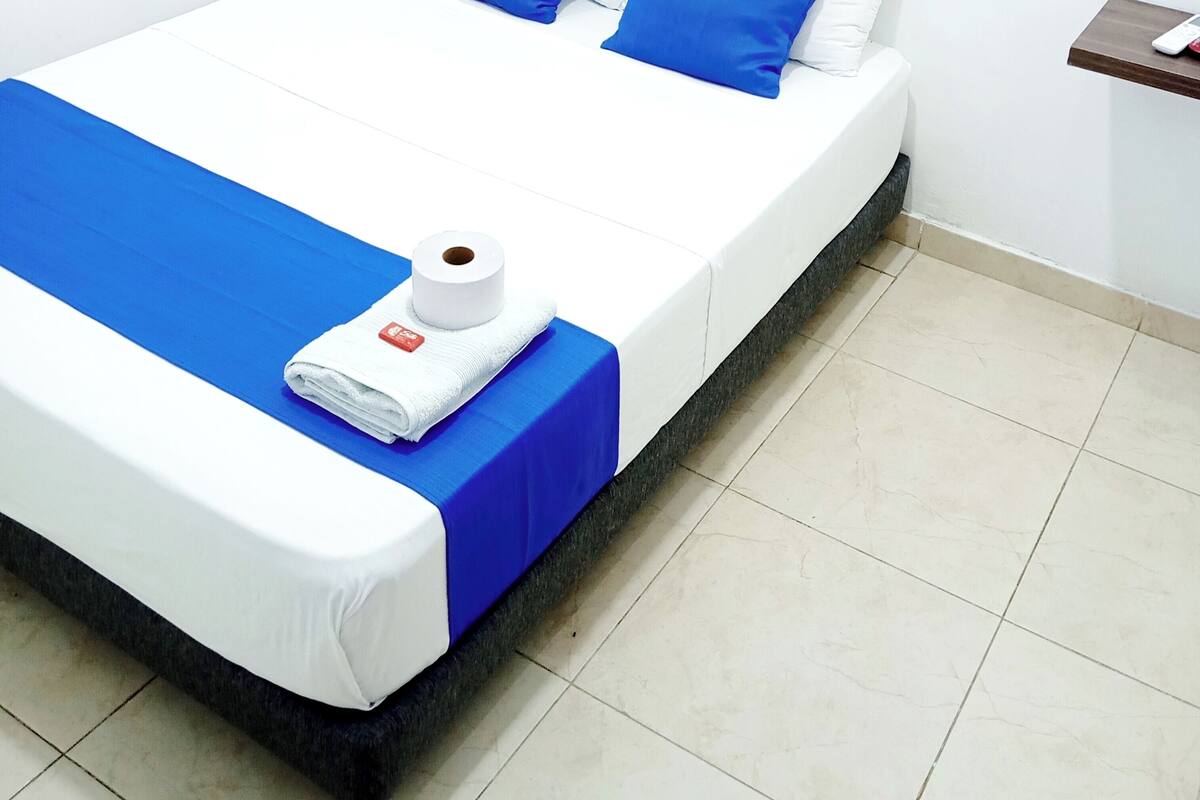 A neatly made bed with blue and white bedding, a white towel, and a roll of toilet paper on the bed.