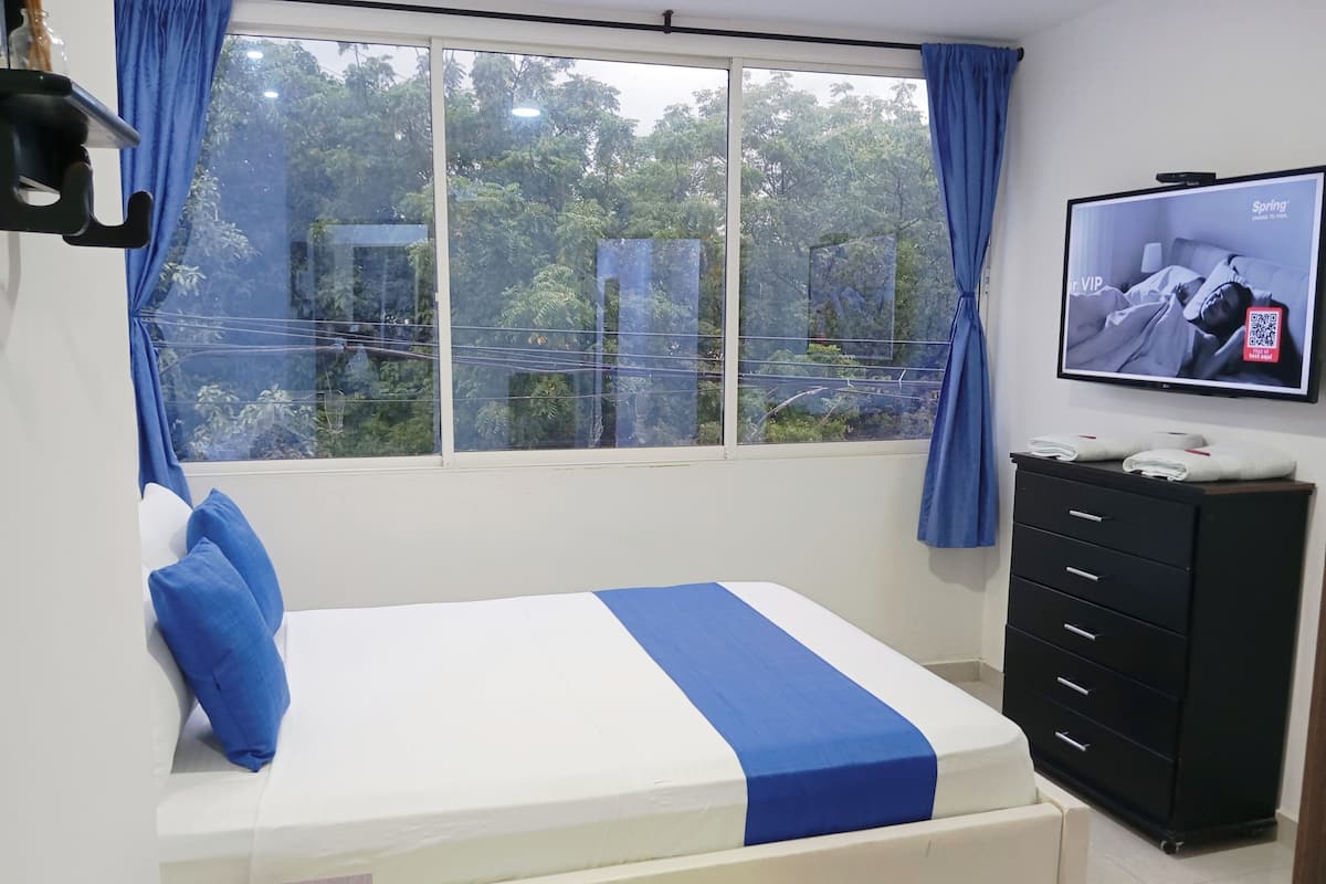 A hotel room with a bed, a TV, a dresser, and a window with curtains.