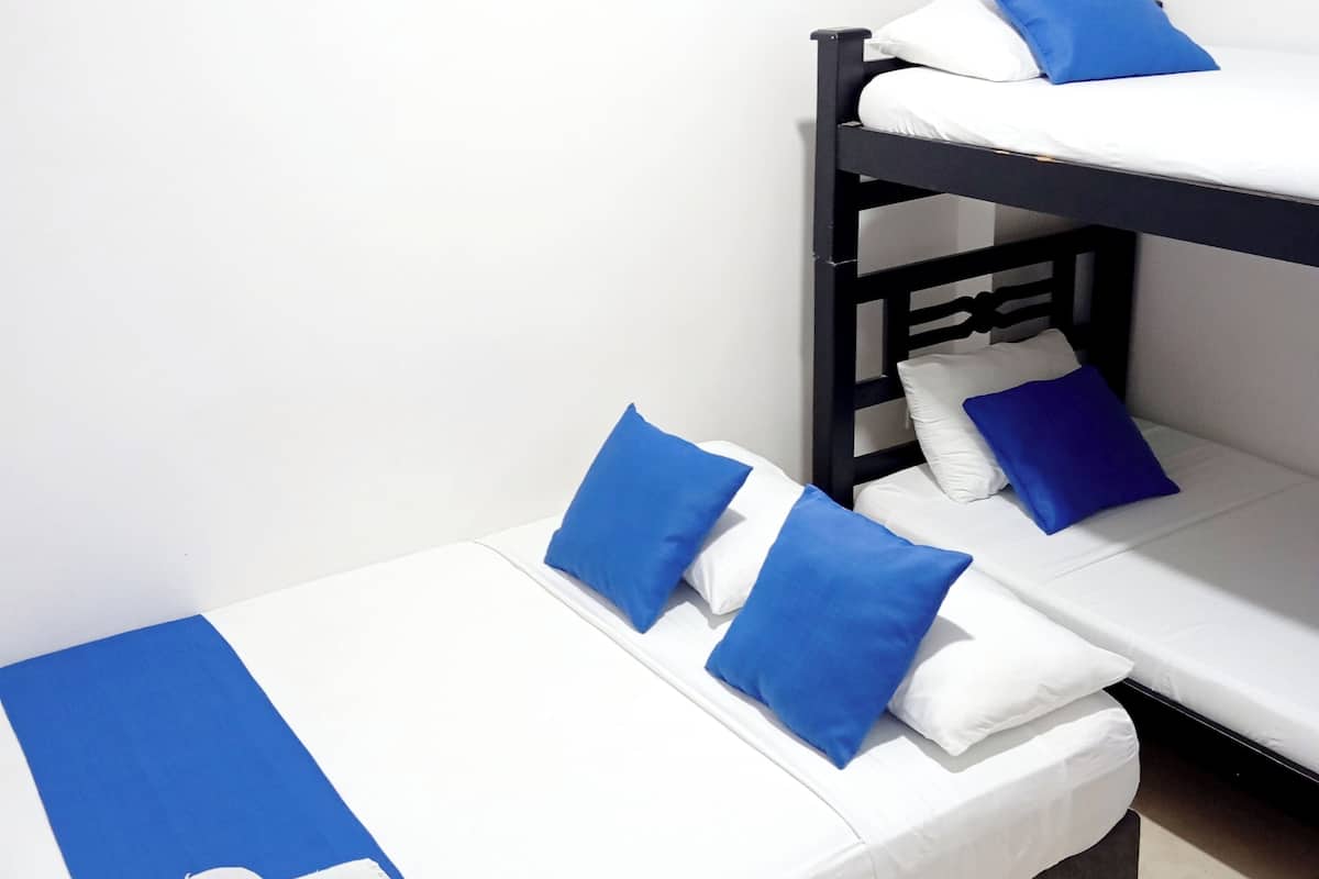 A bunk bed room with a white wall, a white air conditioning unit, and a blue towel on the lower bunk.
