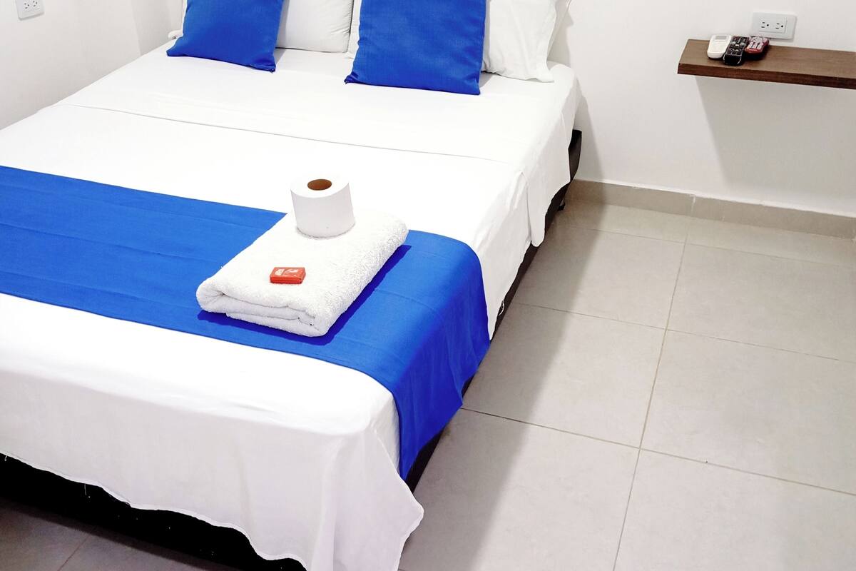 A neatly made bed with blue and white bedding, a white towel, and a red object on the bed.