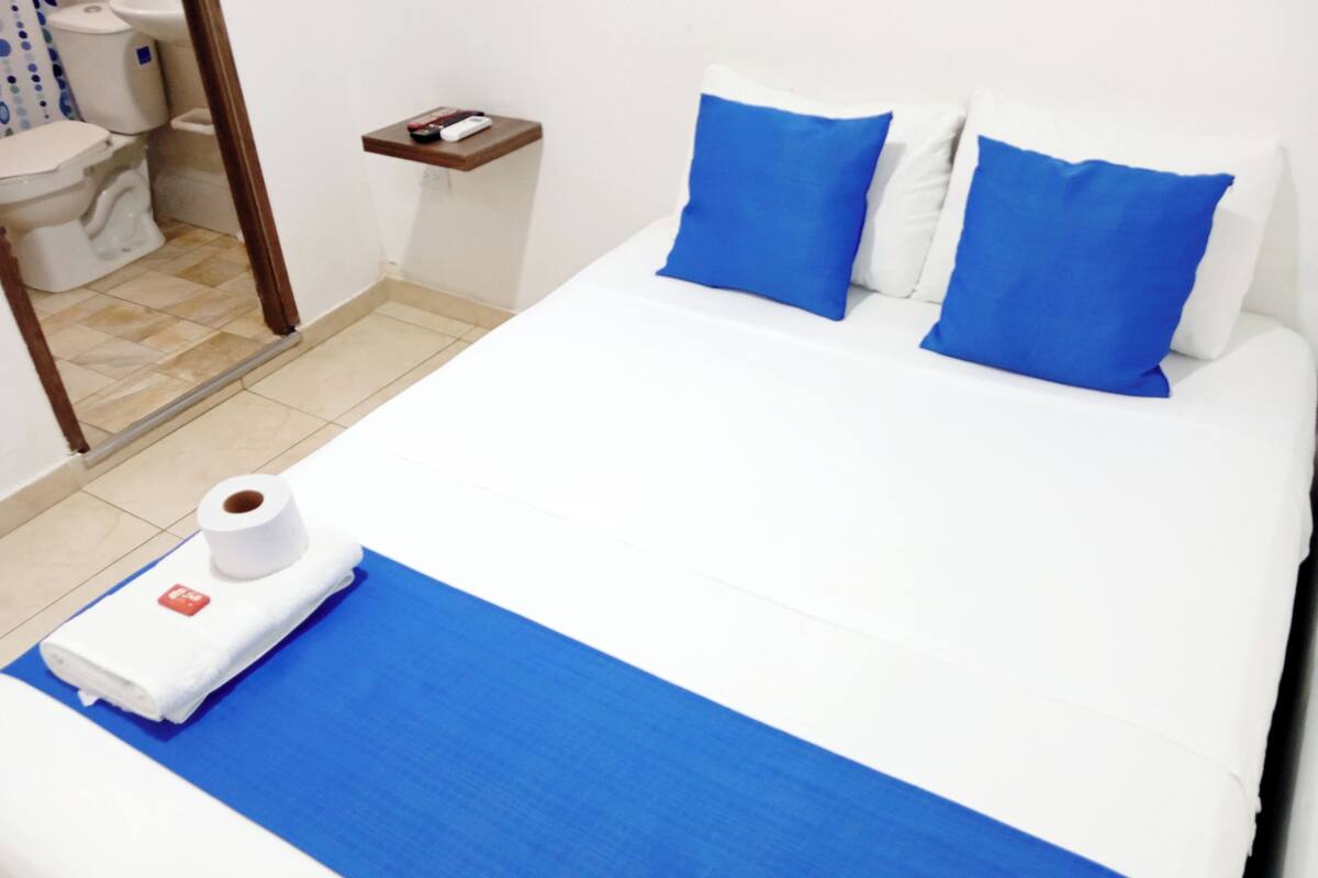 A hotel room with a bed, a small bedside table, a toilet, and a shower area.