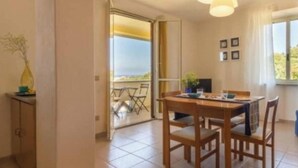 Un comedor con una mesa y sillas, un jarrón en una mesita auxiliar, y vistas a un área de estar exterior a través de un ventanal.