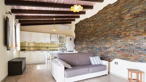 Una sala de estar moderna con un sofá, un taburete de madera y una cocina al fondo.