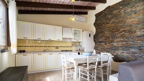Una cocina con armarios blancos, una mesa de comedor con sillas, un tazón azul y una pared de ladrillo.