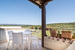 Une terrasse avec une table et des chaises, des plantes en pot et une vue sur la campagne.