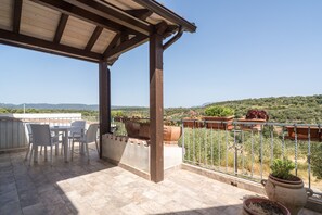 Un espace extérieur abrité, doté d’une terrasse, de chaises blanches et de plantes en pot.