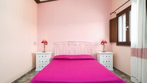 Un dormitori amb un llit, dues taules de nit, una finestra amb cortines i una porta.