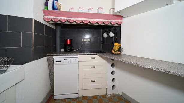 Une cuisine compacte équipée d’un lave-vaisselle, d’une machine à café et d’un torchon à carreaux rouges et blancs posé sur l’évier.