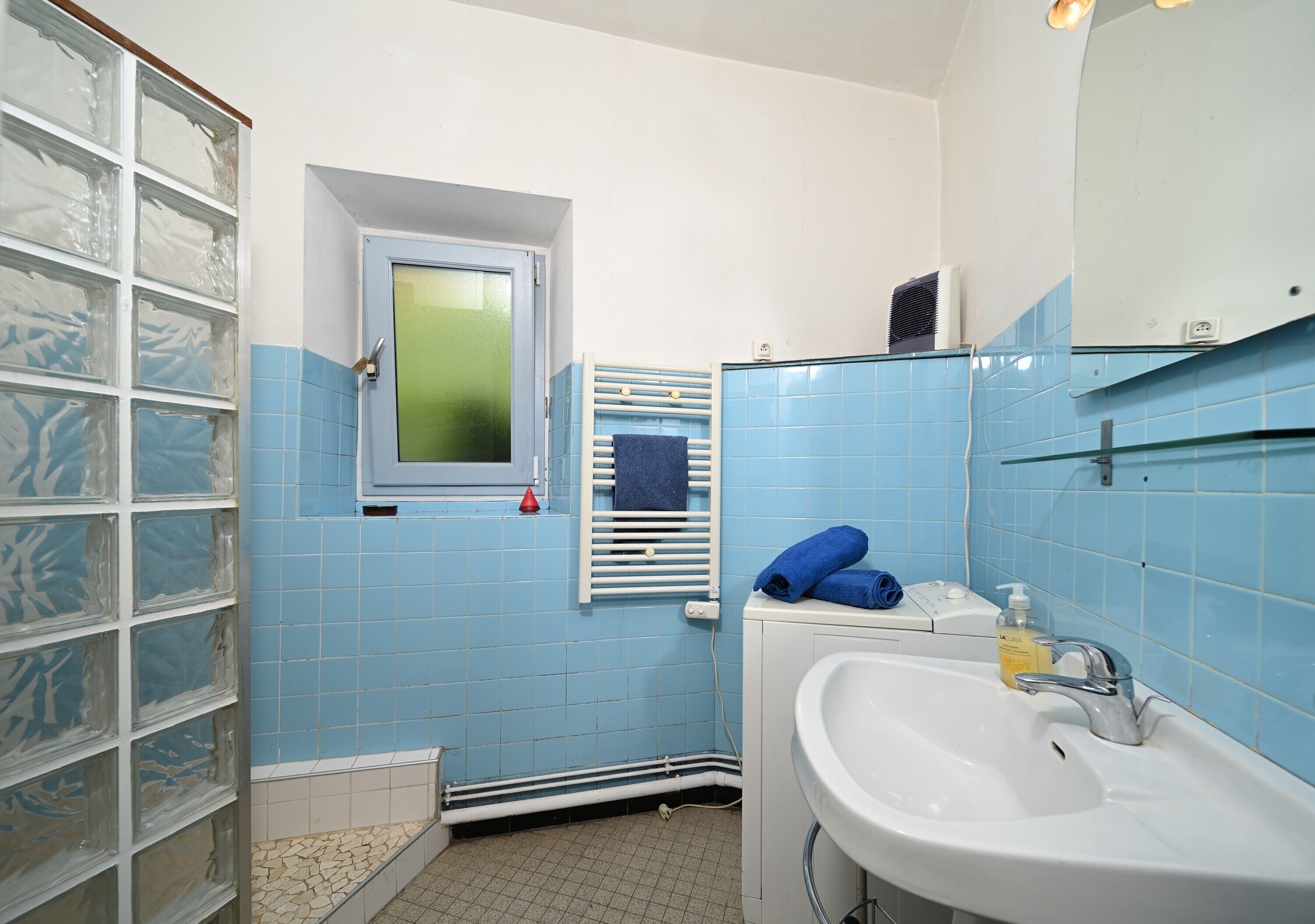 A bathroom with a window, a towel rack, a sink, and a mirror.