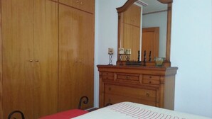 A bedroom with a wooden wardrobe, a dresser with a mirror, and a bed with a white bedspread. - Apartment 'Residencia Lucia' with Sea View, Wi-Fi and Air Conditioning (Guardamar del segura)