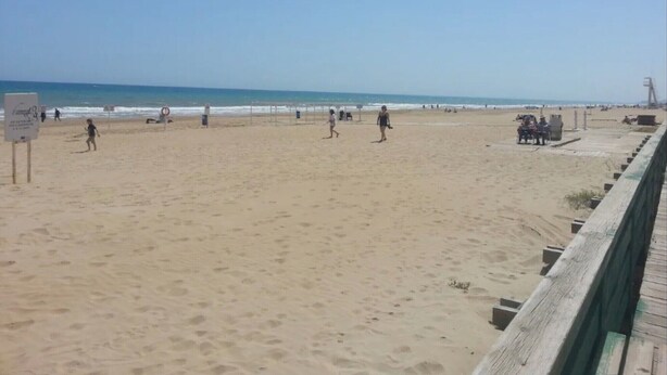 A beach with a wooden boardwalk, people walking, and a lifeguard tower in the distance. - Apartment 'Residencia Lucia' with Sea View, Wi-Fi and Air Conditioning (Guardamar del segura)