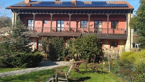 A large, two-story building with a balcony, surrounded by greenery and a gravel path. - Holiday Home 'El Pedrueco Turismo Rural' with Mountain View, Shared Pool and Wi-Fi (Nava)