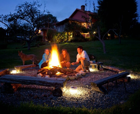 A group of people around a campfire with a house in the background.