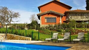 A swimming pool with lounge chairs, a stone wall, and a house with a red facade. - Holiday Home 'El Pedrueco Turismo Rural' with Mountain View, Shared Pool and Wi-Fi (Nava)
