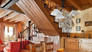 A rustic interior with a wooden staircase, a dining area with a table and chairs, and a kitchen area with cabinets and a hanging light fixture. - Holiday Home 'El Pedrueco Turismo Rural' with Mountain View, Shared Pool and Wi-Fi (Nava)