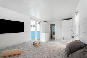A bedroom with a bed, a TV, a bathroom, and a view of the outside.