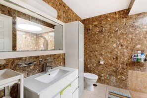 Un baño con pared de mármol, lavamanos blanco, espejo y retrete.
