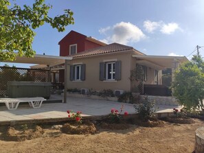A two-story house with a red roof, a covered patio, and a garden with red flowers.