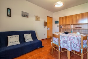 Un salon avec un canapé bleu foncé, une table recouverte d’une nappe à motifs et des meubles en bois.