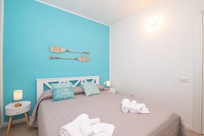 A bedroom with a bed, pillows, a wall-mounted paddle, a nightstand, and a lamp. - Apartment 'Villa Clelia' with Private Terrace, Private Garden, Air Conditioning and Wi-Fi (Palau)