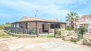 Une maison de plain-pied avec un toit en tuiles, une véranda et un mur en pierre.