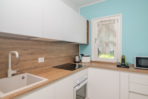 A modern kitchen with a wooden countertop, white cabinets, a built-in oven, and a window with a decorative curtain. - Apartment 'Villa Clelia' with Private Terrace, Private Garden, Air Conditioning and Wi-Fi (Palau)