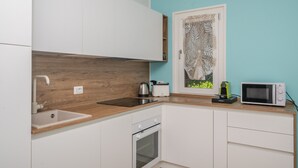Une cuisine avec des armoires blanches, un plan de travail en bois, un évier, une cuisinière et un four à micro-ondes.