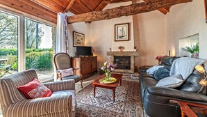 A cozy living room with a fireplace, a television, and a large window overlooking greenery. - Cottage 'Gîte Calme Avec Jardin Et Terrasse' with Private Terrace, Private Garden and Wi-Fi (Guiclan)