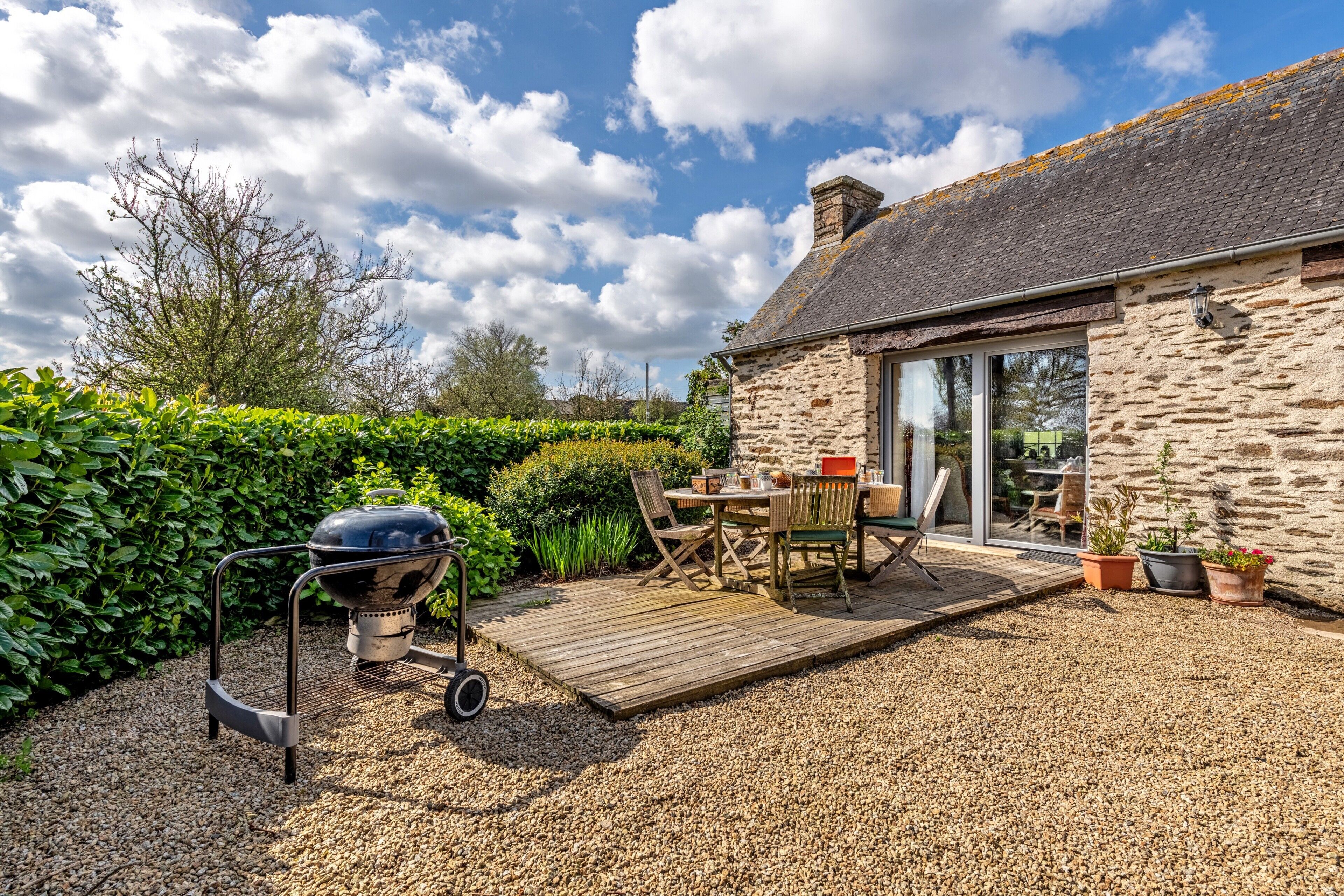 A patio with a grill, outdoor furniture, and a stone building with a glass door.