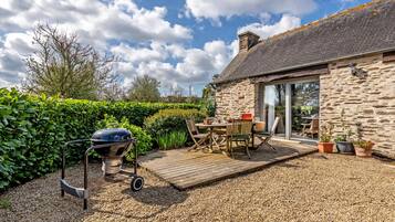 A patio with a grill, outdoor furniture, and a stone building with a glass door.