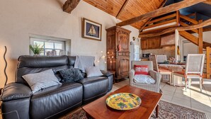 A cozy living room with a leather sofa, wooden dining table, and a kitchen area. - Cottage 'Gîte Calme Avec Jardin Et Terrasse' with Private Terrace, Private Garden and Wi-Fi (Guiclan)