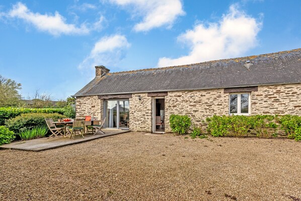 A stone building with a gravel driveway, a wooden deck, and a patio with outdoor furniture. - Cottage 'Gîte Calme Avec Jardin Et Terrasse' with Private Terrace, Private Garden and Wi-Fi (Guiclan)