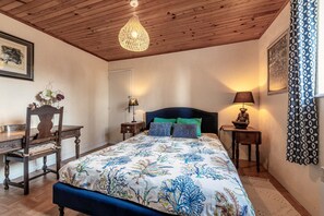 A bedroom with a wooden ceiling, a bed with a floral bedspread, a desk with a chair, and a nightstand with a lamp. - Cottage 'Gîte Calme Avec Jardin Et Terrasse' with Private Terrace, Private Garden and Wi-Fi (Guiclan)