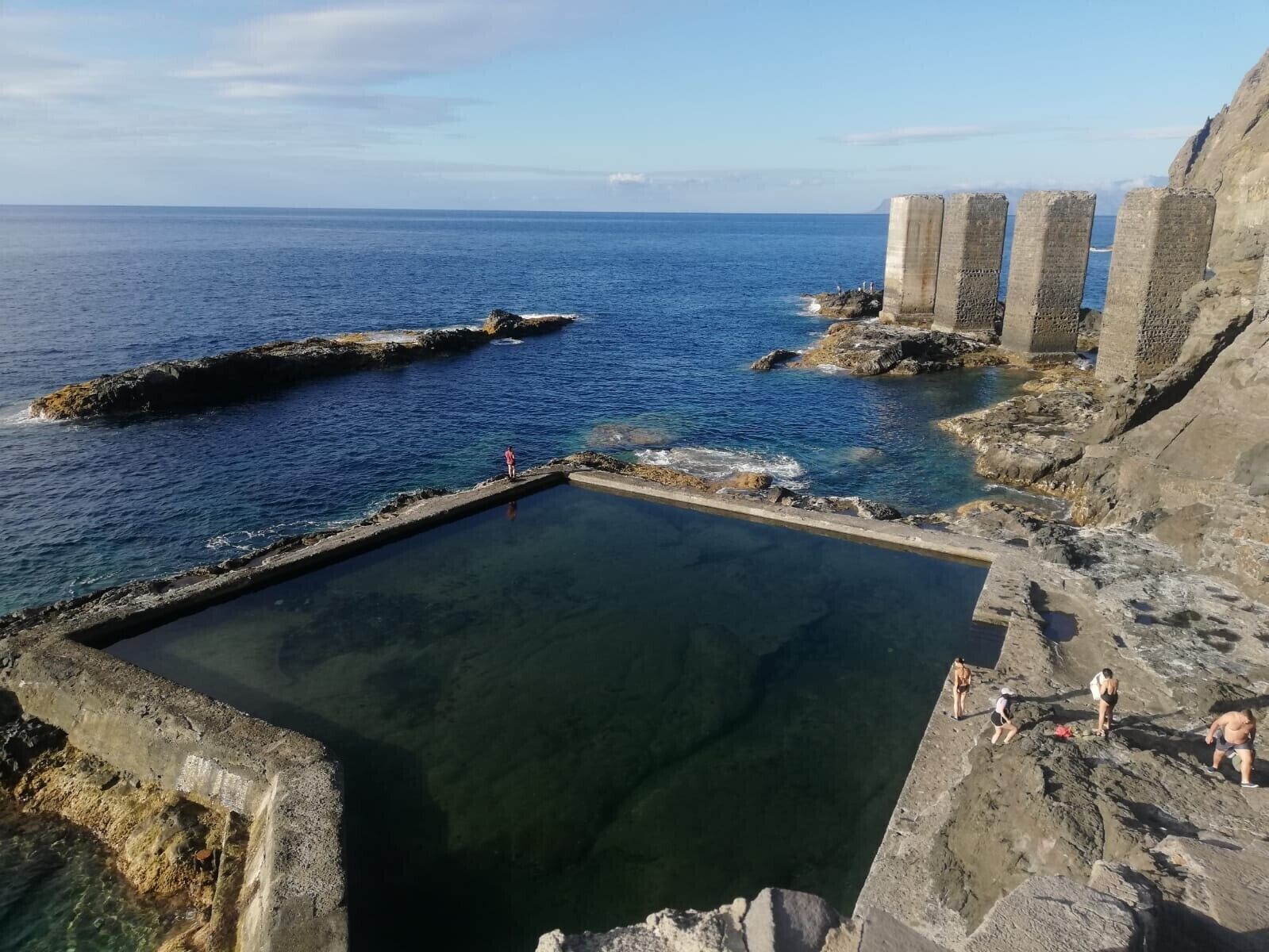 A coastal scene with a clear pool, rocky terrain, and a distant view of the ocean.