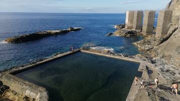 A coastal scene with a clear pool, rocky terrain, and a distant view of the ocean.