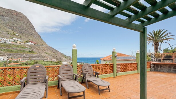 A terrace with two lounge chairs, a pergola, and a view of a coastal village. - Holiday Home 'Casa Rural Ondina A' with Sea View, Private Terrace and Wi-Fi (Hermigua)