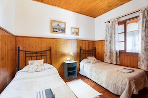 Ein Zimmer mit zwei Betten, Holzwänden, einem kleinen Tisch mit einer Lampe und einem Fenster mit Vorhängen.