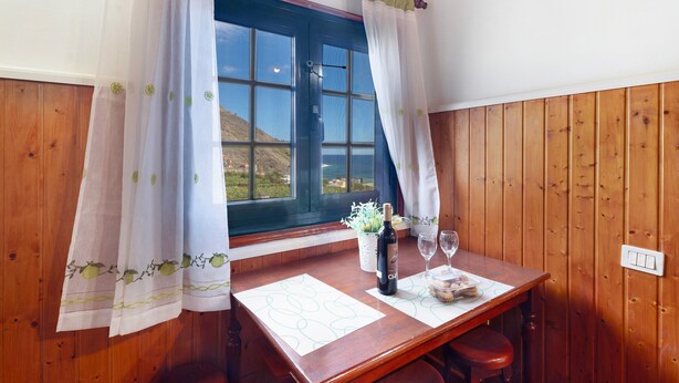 Ein Zimmer mit Holzwänden, einem Fenster, einem Tisch mit Flasche und Gläsern sowie einem Blumentopf.