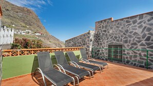 Eine Dachterrasse mit vier Liegestühlen, einer Steinmauer und Blick auf ein Hügeldorf.