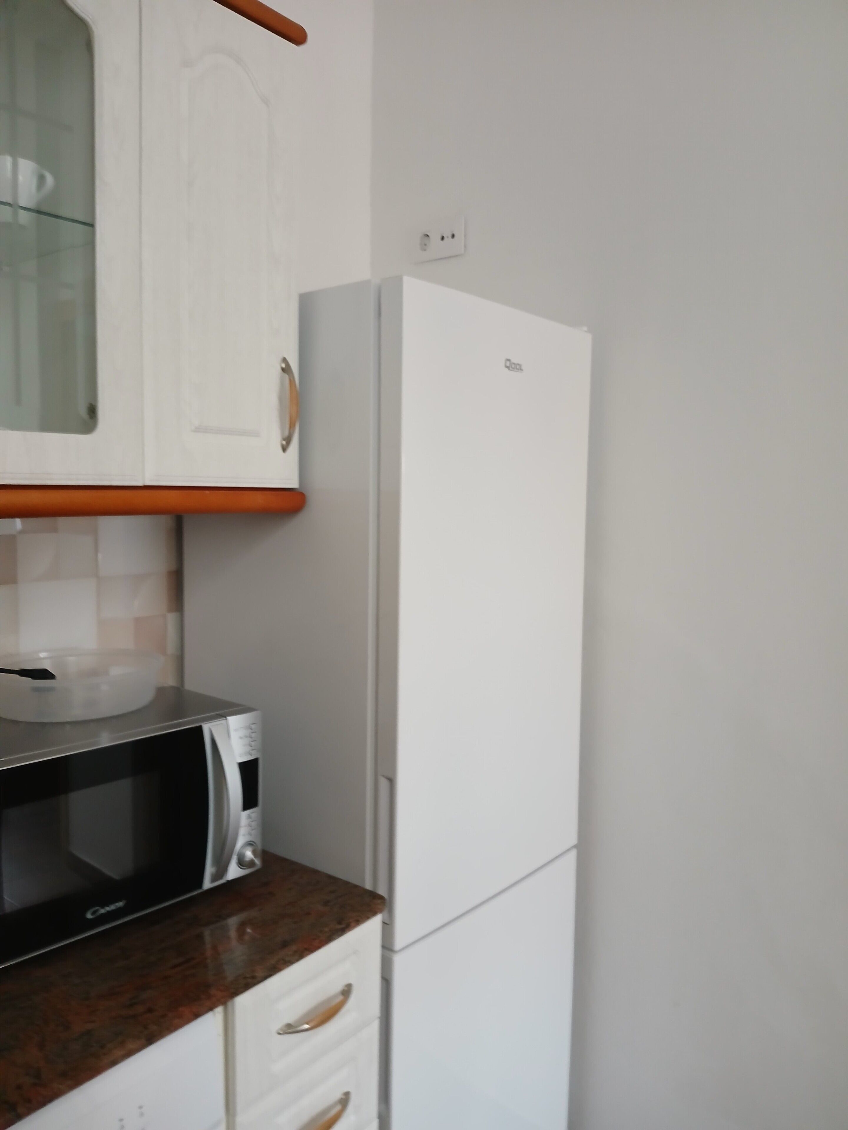 Cuina amb microones, nevera blanca i un armari amb porta de vidre.