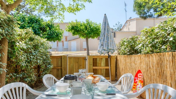 Mesa dispuesta al aire libre con sillas blancas, mantel y diversos platos y utensilios.