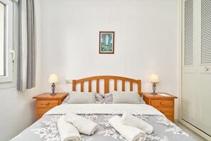 A neatly made bed with a floral bedspread, two bedside tables with lamps, a framed picture on the wall, and a window with curtains.