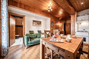A wooden-paneled room with a dining table, a green sofa, and a kitchen area.