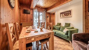 A wooden interior with a dining table, chairs, a green sofa, and a clock on the wall.