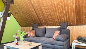 A cozy living room with a sloped ceiling, a grey sofa with patterned cushions, a wooden coffee table, and a small white side table. - Kranich by Interhome (Lübz)