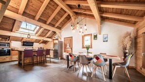 A spacious kitchen with wooden beams, a dining area with chairs, and a large window.