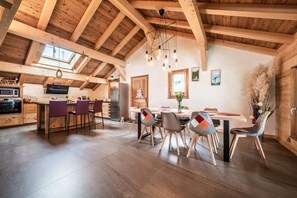 Une cuisine spacieuse avec des poutres en bois, un coin repas avec des chaises et une grande fenêtre.